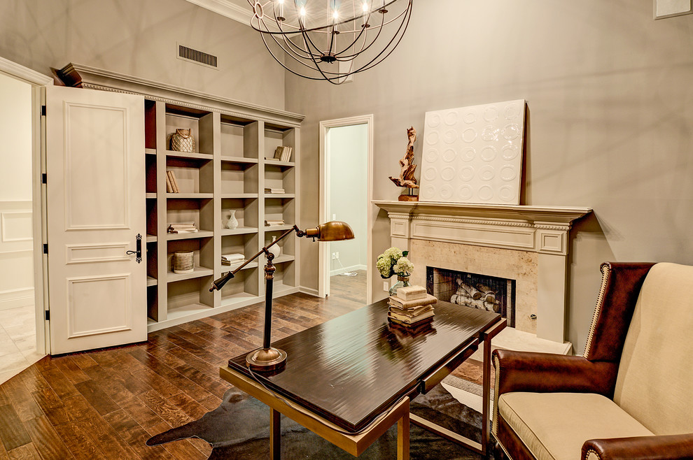Inspiration för stora klassiska hemmabibliotek, med grå väggar, mörkt trägolv, en standard öppen spis, en spiselkrans i trä, ett fristående skrivbord och brunt golv