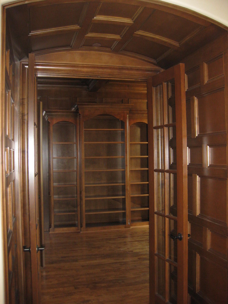 Diseño de despacho clásico grande con biblioteca, paredes marrones y suelo de madera oscura