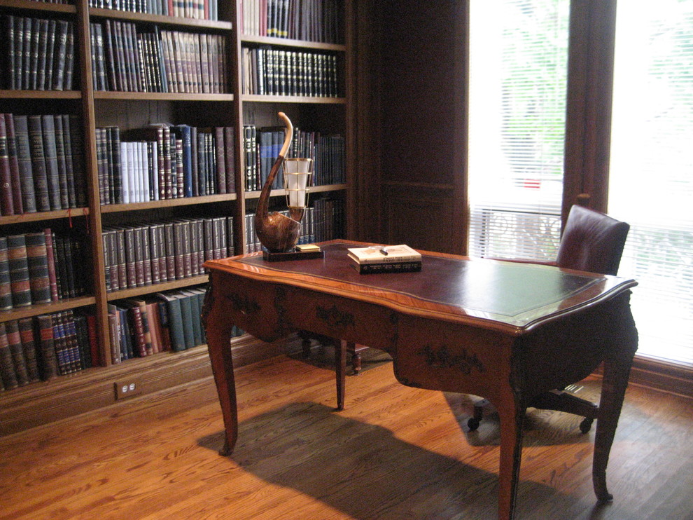 Klassisk inredning av ett stort hemmabibliotek, med bruna väggar, mellanmörkt trägolv och ett fristående skrivbord