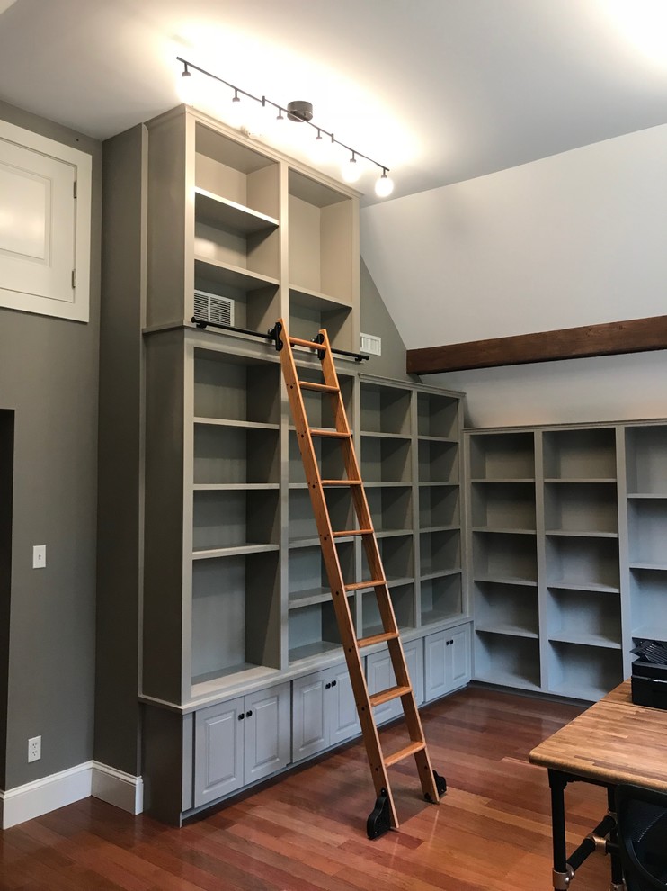 Cette image montre un bureau craftsman de taille moyenne avec une bibliothèque ou un coin lecture, un mur gris, un sol en bois brun et un sol rouge.