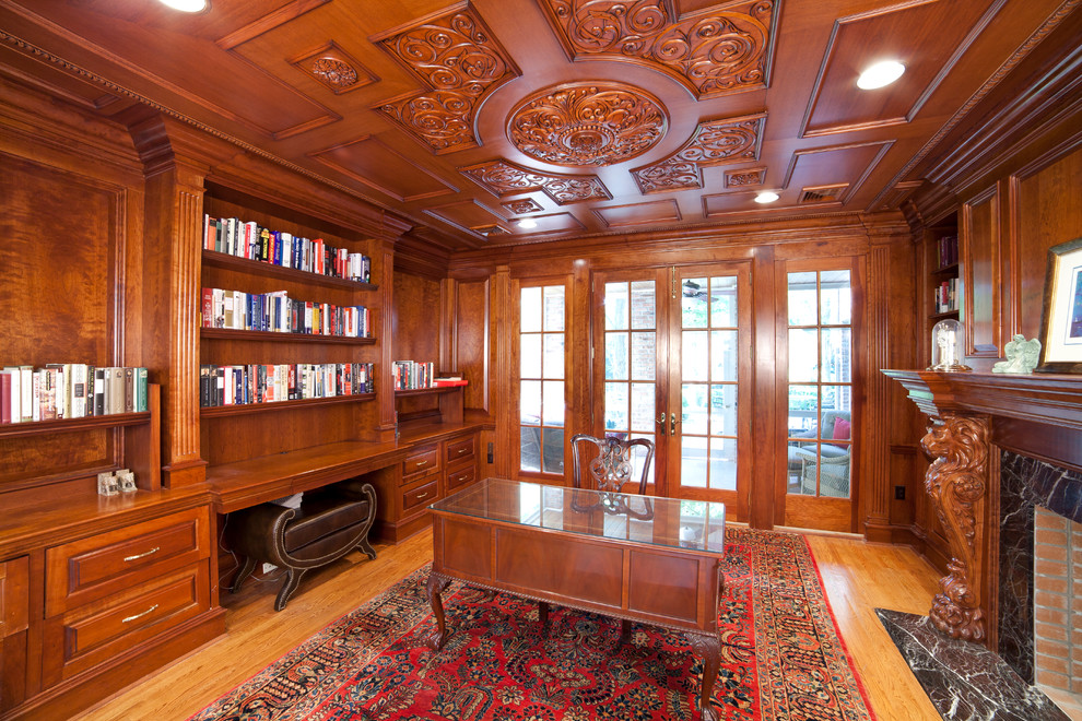 Klassisk inredning av ett mellanstort hemmabibliotek, med bruna väggar, mellanmörkt trägolv, en standard öppen spis, en spiselkrans i sten, ett fristående skrivbord och brunt golv