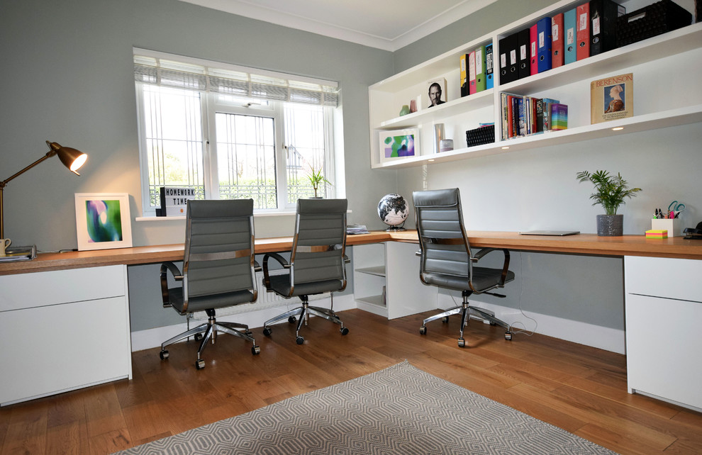 Foto de despacho actual grande con paredes grises, suelo de madera en tonos medios, escritorio empotrado y suelo marrón