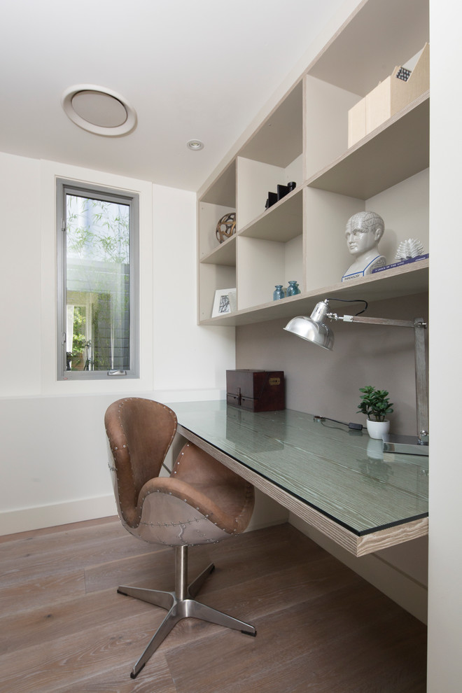 Modelo de despacho actual pequeño con paredes blancas, suelo de madera en tonos medios y escritorio empotrado
