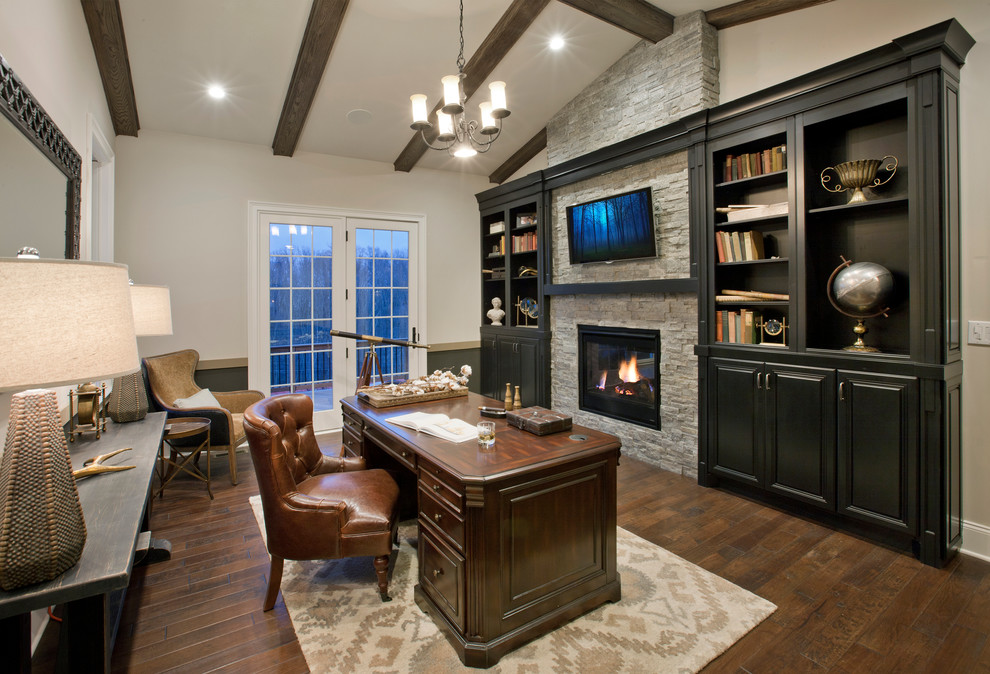 Imagen de despacho tradicional con paredes grises, suelo de madera oscura, todas las chimeneas, marco de chimenea de piedra y escritorio independiente