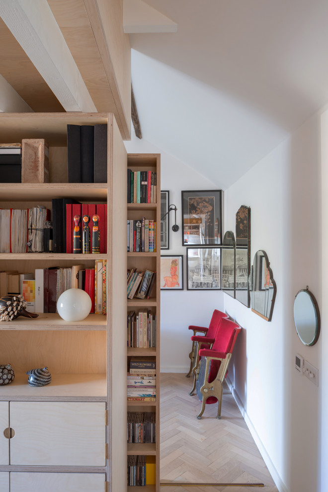 Modelo de despacho nórdico pequeño sin chimenea con paredes blancas, suelo de madera clara, escritorio empotrado, suelo marrón y vigas vistas