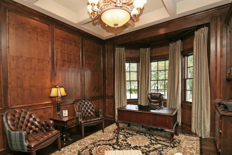 Großes Klassisches Arbeitszimmer mit Arbeitsplatz, brauner Wandfarbe, dunklem Holzboden, Kamin, Kaminumrandung aus Stein, freistehendem Schreibtisch und braunem Boden in Austin