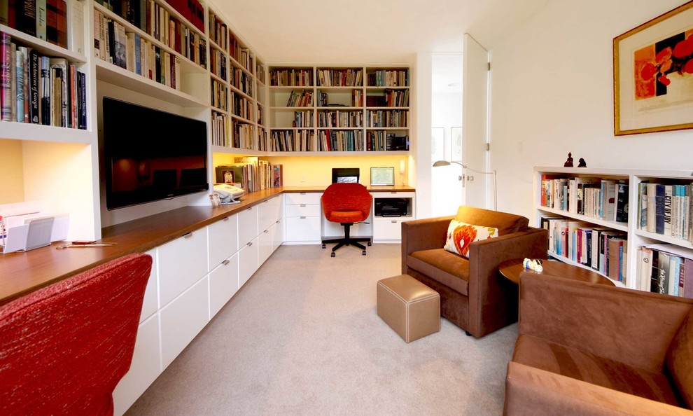 На фото: домашняя библиотека среднего размера в стиле ретро с белыми стенами, ковровым покрытием, встроенным рабочим столом и серым полом без камина с