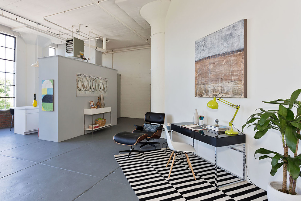 Foto di uno studio industriale con pareti bianche, pavimento in cemento e scrivania autoportante