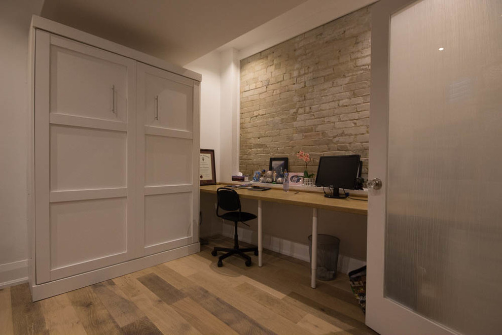 Foto på ett litet funkis arbetsrum, med ett bibliotek, vita väggar, laminatgolv, ett inbyggt skrivbord och brunt golv