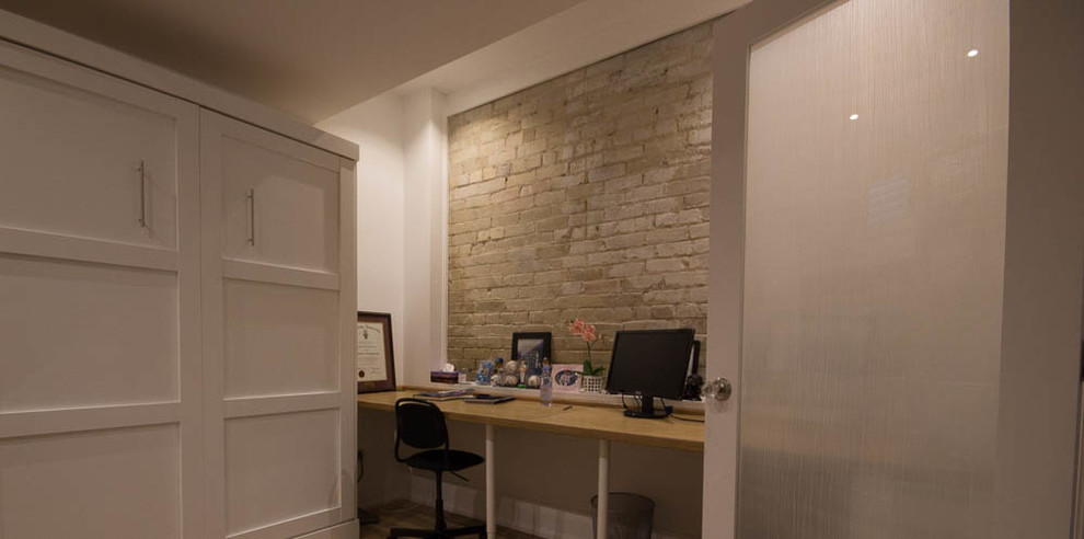 Modelo de despacho actual pequeño con biblioteca, paredes blancas, suelo laminado, escritorio empotrado y suelo marrón