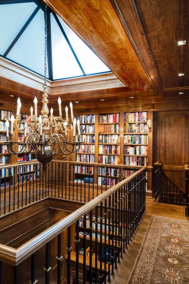 Imagen de despacho clásico renovado extra grande sin chimenea con biblioteca, paredes marrones, suelo de madera en tonos medios y escritorio empotrado