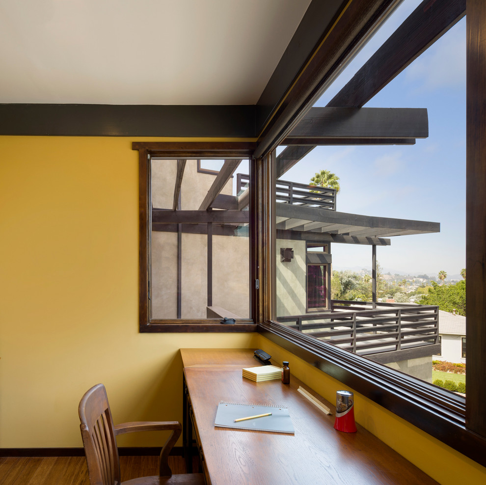 ロサンゼルスにあるコンテンポラリースタイルのおしゃれなホームオフィス・書斎 (黄色い壁、濃色無垢フローリング、造り付け机) の写真