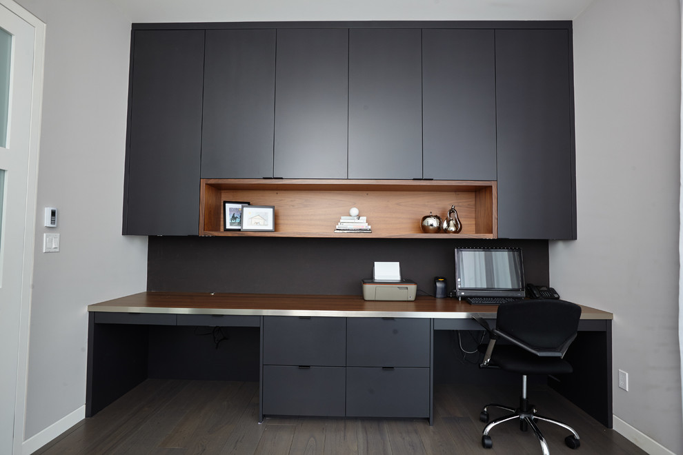 This is an example of a medium sized modern home office in Toronto with grey walls, medium hardwood flooring, no fireplace, a built-in desk and brown floors.