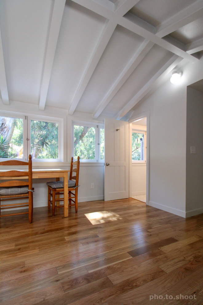 Cette image montre un bureau atelier traditionnel de taille moyenne avec un mur blanc, un sol en bois brun, un bureau indépendant, un sol marron et poutres apparentes.