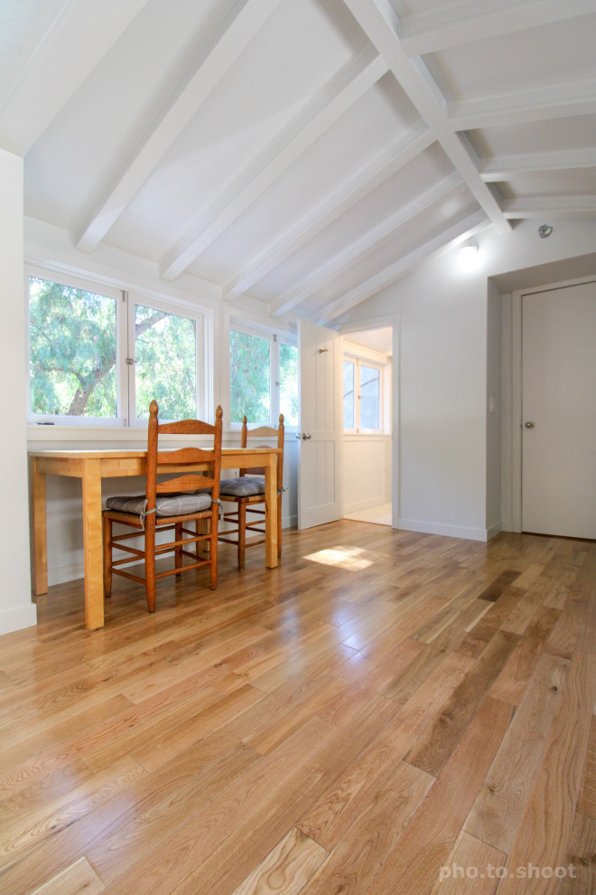 Cette photo montre un bureau atelier chic de taille moyenne avec un mur blanc, un sol en bois brun, un bureau indépendant, un sol marron et poutres apparentes.