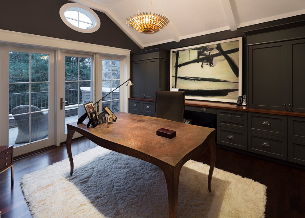 Klassisk inredning av ett mellanstort arbetsrum, med ett bibliotek, mörkt trägolv, ett fristående skrivbord och brunt golv