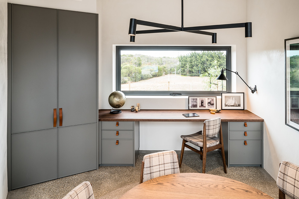 This is an example of a small contemporary study in Melbourne with white walls, concrete flooring, a built-in desk and grey floors.