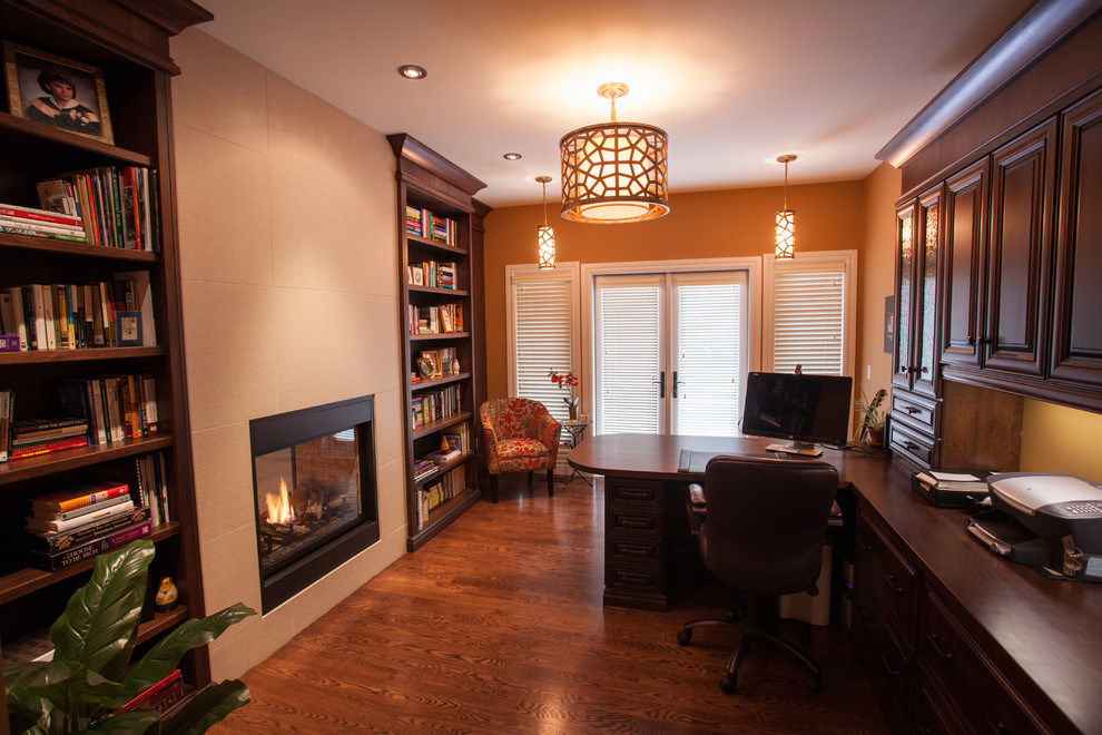Inspiration for a medium sized traditional study in Calgary with medium hardwood flooring, a ribbon fireplace, a built-in desk and orange walls.