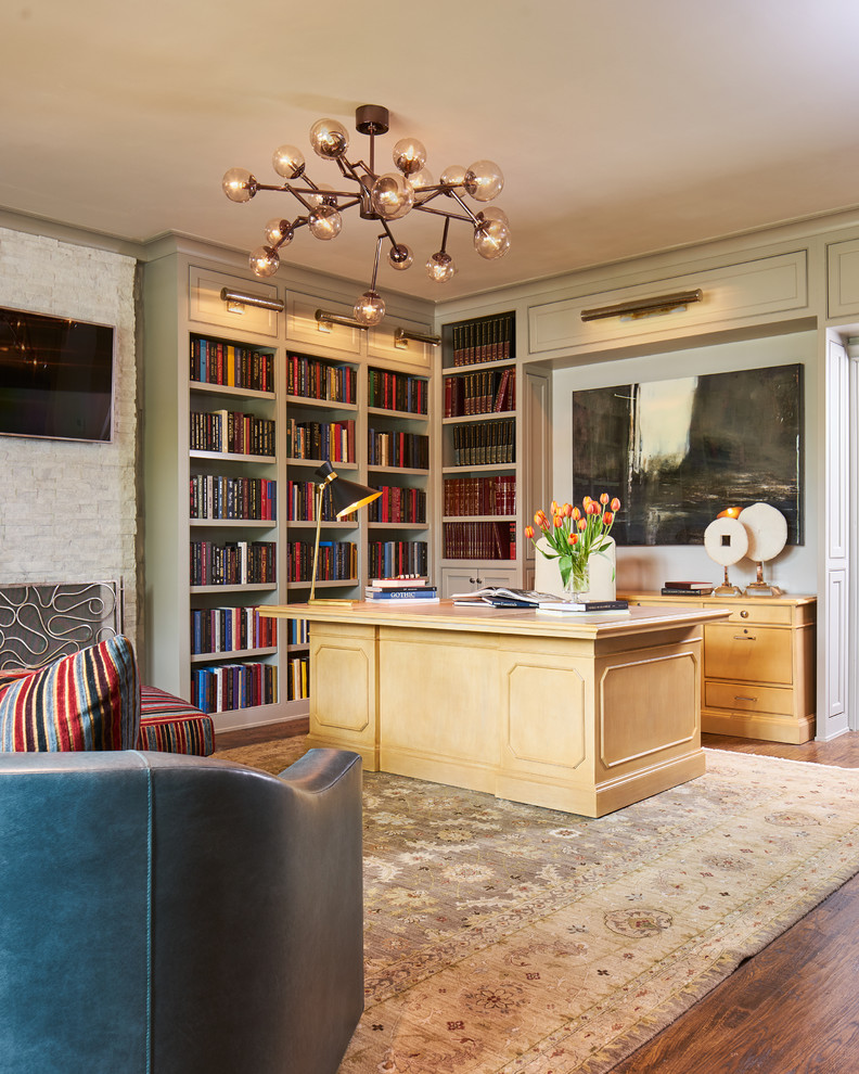 Inredning av ett klassiskt stort hemmabibliotek, med grå väggar, mellanmörkt trägolv, en standard öppen spis, en spiselkrans i sten, ett fristående skrivbord och brunt golv