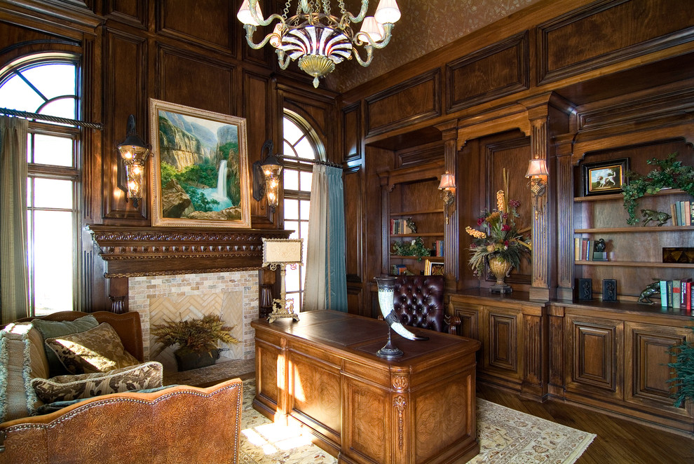 Mittelgroßes Klassisches Arbeitszimmer mit Arbeitsplatz, freistehendem Schreibtisch, dunklem Holzboden, Kaminumrandung aus Stein, brauner Wandfarbe und Kamin in Chicago
