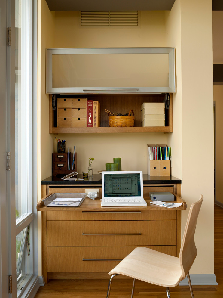 60 tals inredning av ett litet hemmabibliotek, med beige väggar, mellanmörkt trägolv och ett inbyggt skrivbord