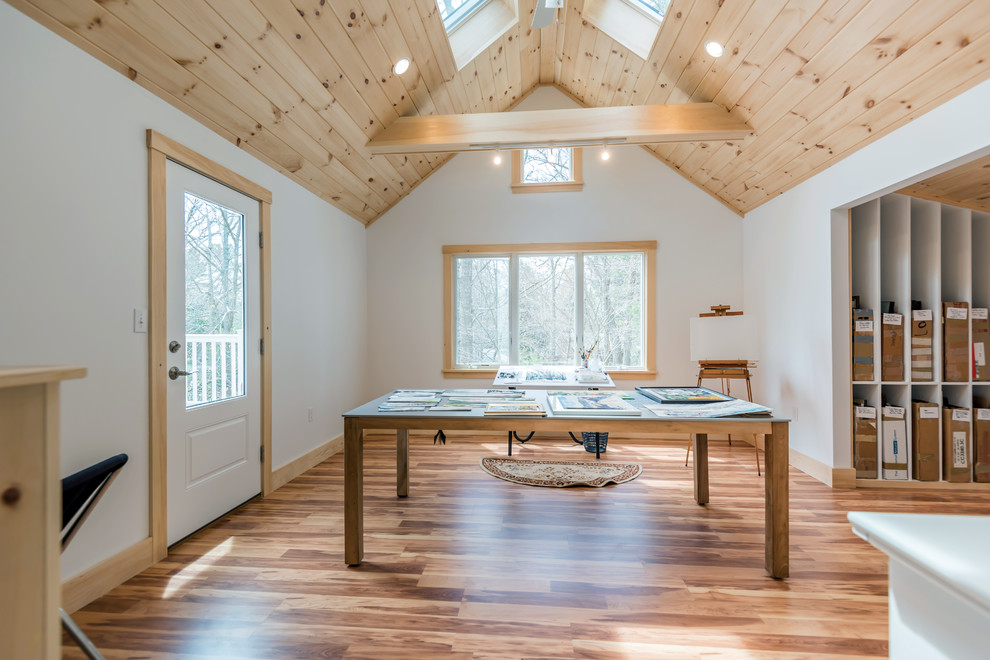 Modelo de estudio actual de tamaño medio con paredes blancas, suelo de madera en tonos medios, escritorio independiente y suelo marrón