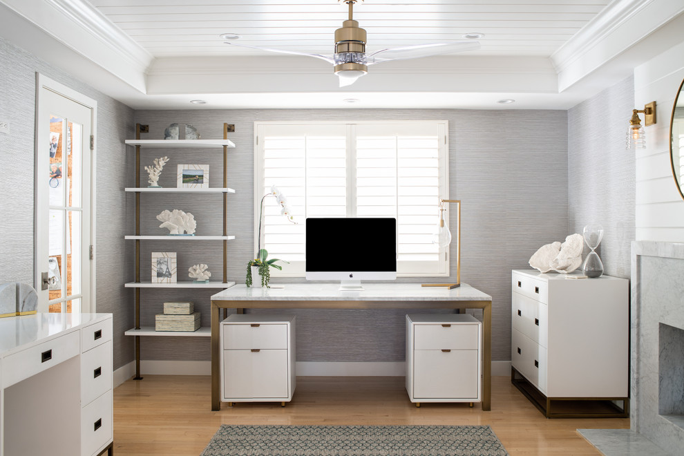 This is an example of a medium sized coastal home office in Los Angeles with grey walls, light hardwood flooring, a stone fireplace surround, a freestanding desk, a timber clad ceiling, a drop ceiling, beige floors and wallpapered walls.