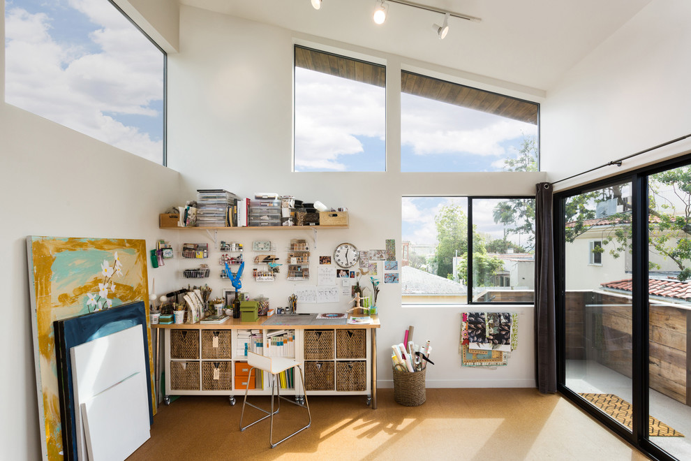 Foto de estudio contemporáneo pequeño sin chimenea con suelo de corcho, suelo marrón, paredes blancas y escritorio independiente