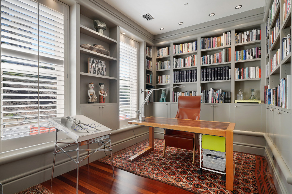Стильный дизайн: большой домашняя библиотека в стиле фьюжн с серыми стенами, паркетным полом среднего тона и отдельно стоящим рабочим столом без камина - последний тренд