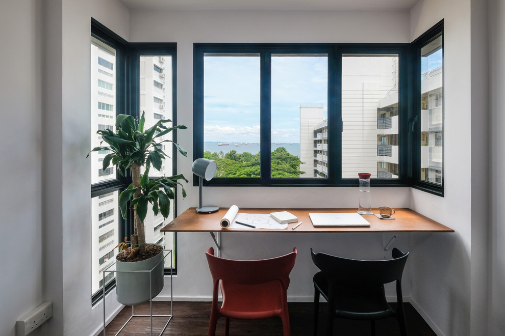Modernes Arbeitszimmer mit weißer Wandfarbe, dunklem Holzboden, Einbau-Schreibtisch und braunem Boden in Singapur