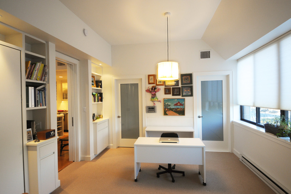 Bild på ett funkis arbetsrum, med vita väggar, heltäckningsmatta och ett fristående skrivbord