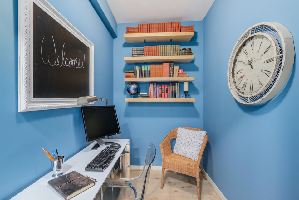 Modern inredning av ett litet hemmabibliotek, med blå väggar, ljust trägolv och ett fristående skrivbord