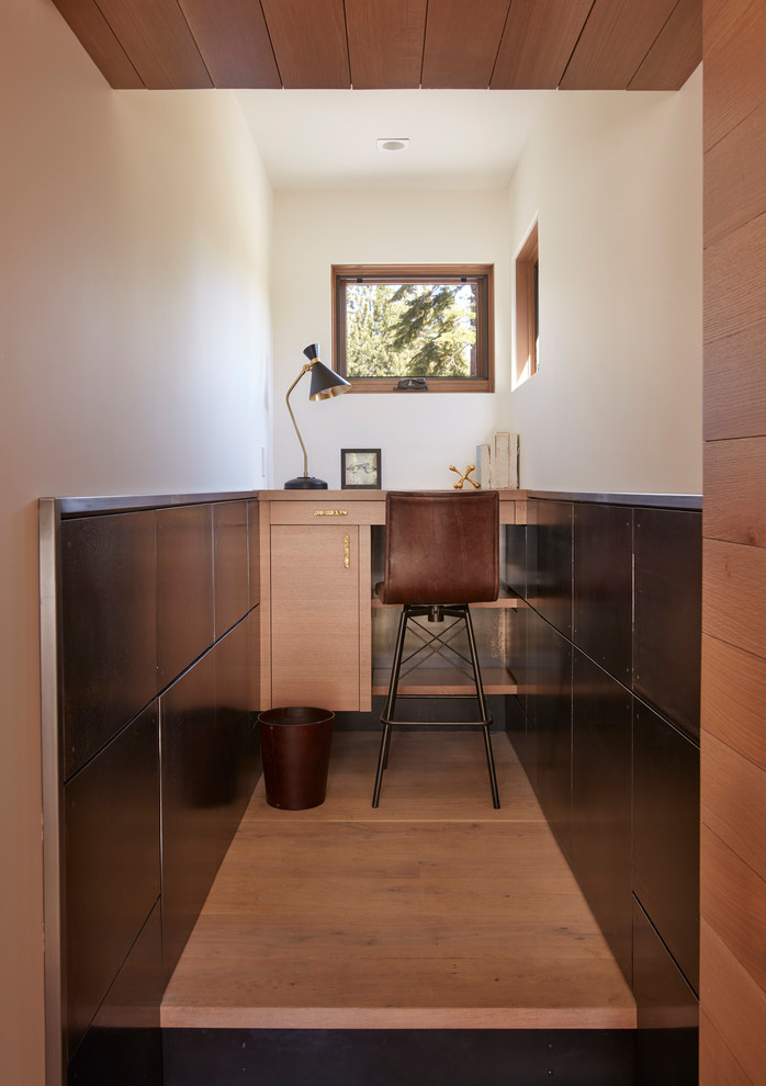 Modern inredning av ett litet hemmabibliotek, med vita väggar, mellanmörkt trägolv, ett inbyggt skrivbord och brunt golv