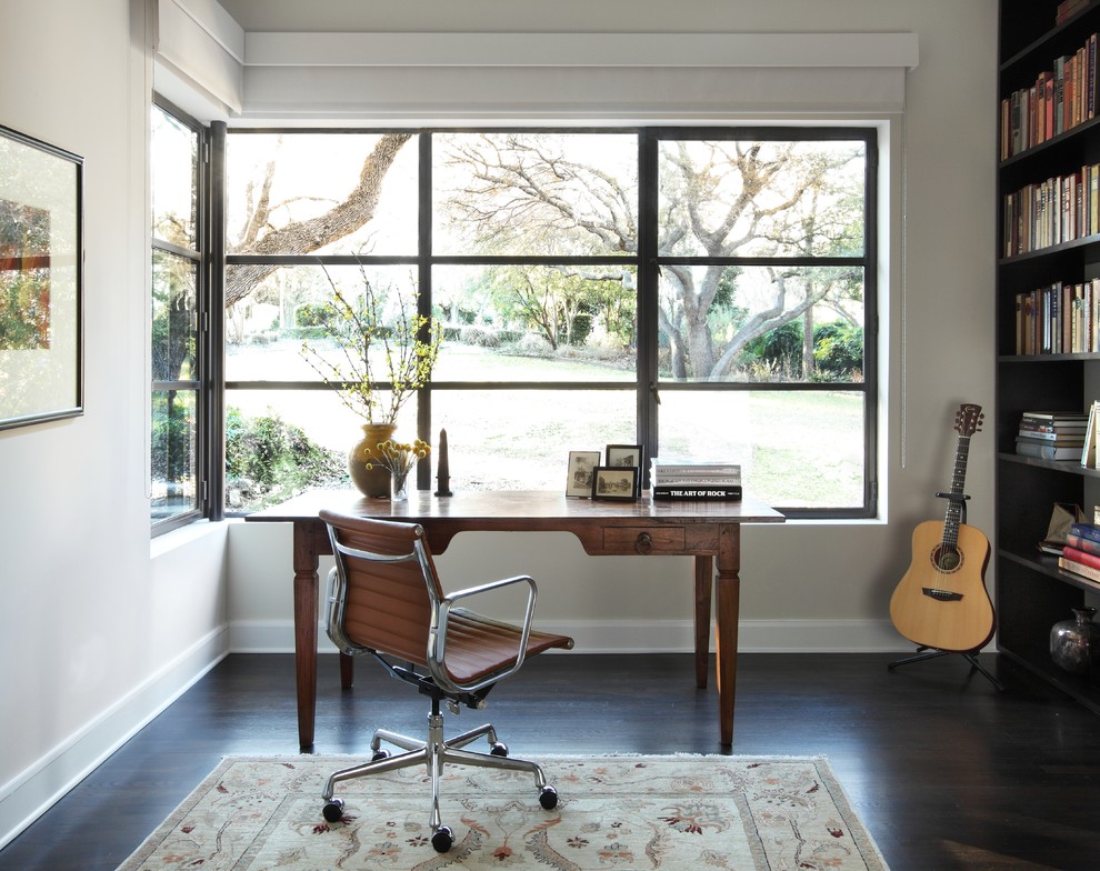 Modernes Arbeitszimmer mit weißer Wandfarbe, dunklem Holzboden, freistehendem Schreibtisch und braunem Boden in Austin