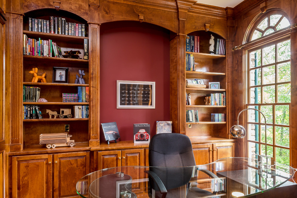 Foto på ett mellanstort funkis hemmabibliotek, med röda väggar, ljust trägolv och ett fristående skrivbord