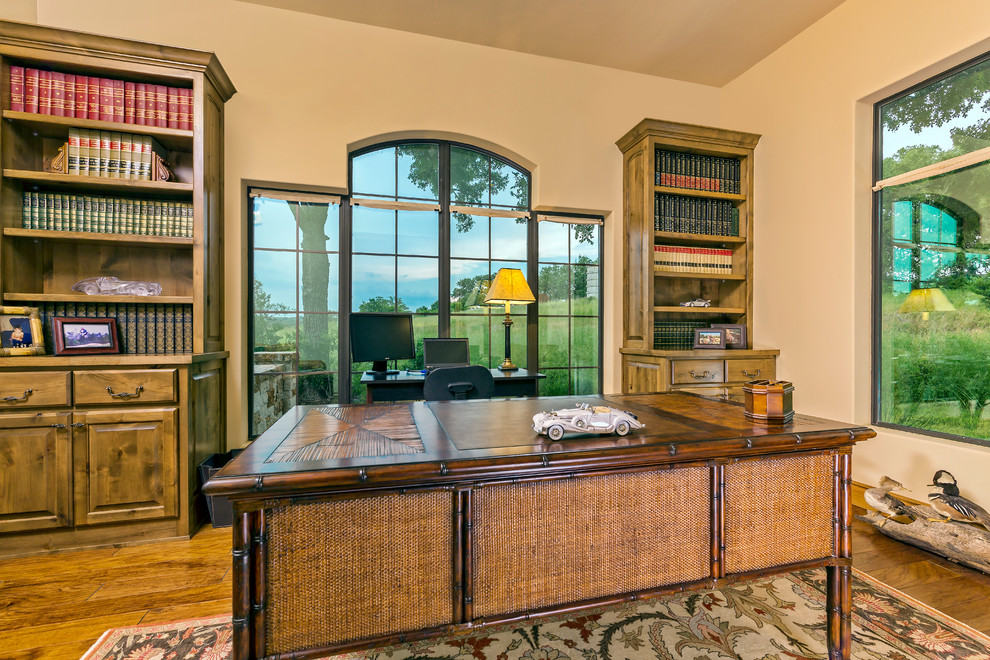 Medelhavsstil inredning av ett stort hemmabibliotek, med beige väggar, mellanmörkt trägolv och ett fristående skrivbord