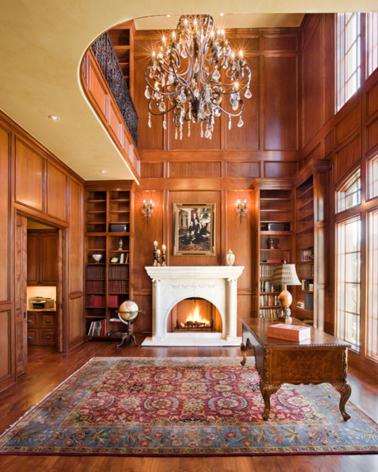 Exempel på ett mycket stort medelhavsstil hemmabibliotek, med beige väggar, mellanmörkt trägolv, en standard öppen spis, en spiselkrans i gips och ett fristående skrivbord