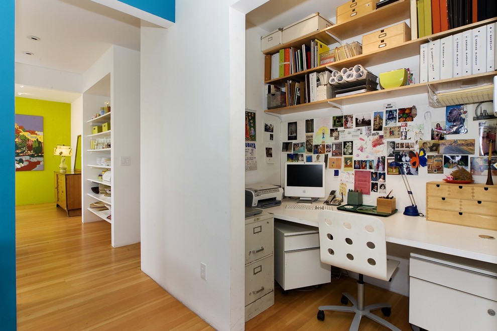 Trendy built-in desk medium tone wood floor home office photo in San Francisco with white walls