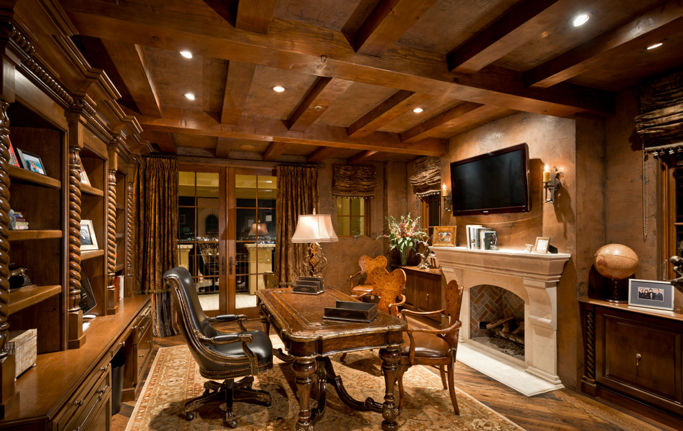 Foto de despacho de estilo americano extra grande con paredes marrones, suelo de madera en tonos medios, todas las chimeneas, marco de chimenea de piedra y escritorio independiente