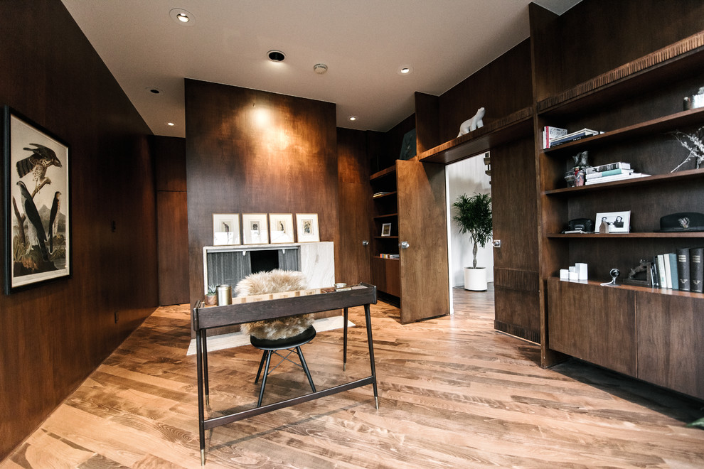 Imagen de despacho actual de tamaño medio con paredes marrones, suelo de madera en tonos medios, todas las chimeneas, marco de chimenea de piedra y escritorio independiente