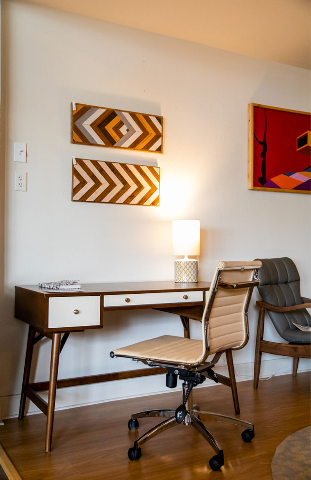 Mittelgroßes Retro Arbeitszimmer mit Arbeitsplatz, weißer Wandfarbe, gebeiztem Holzboden, freistehendem Schreibtisch und braunem Boden in Houston