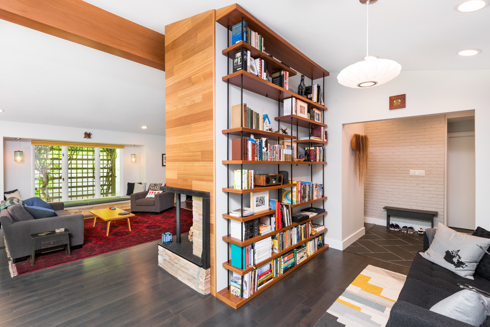 Large mid-century modern dark wood floor and brown floor home office library photo in Detroit with white walls, a brick fireplace and a two-sided fireplace