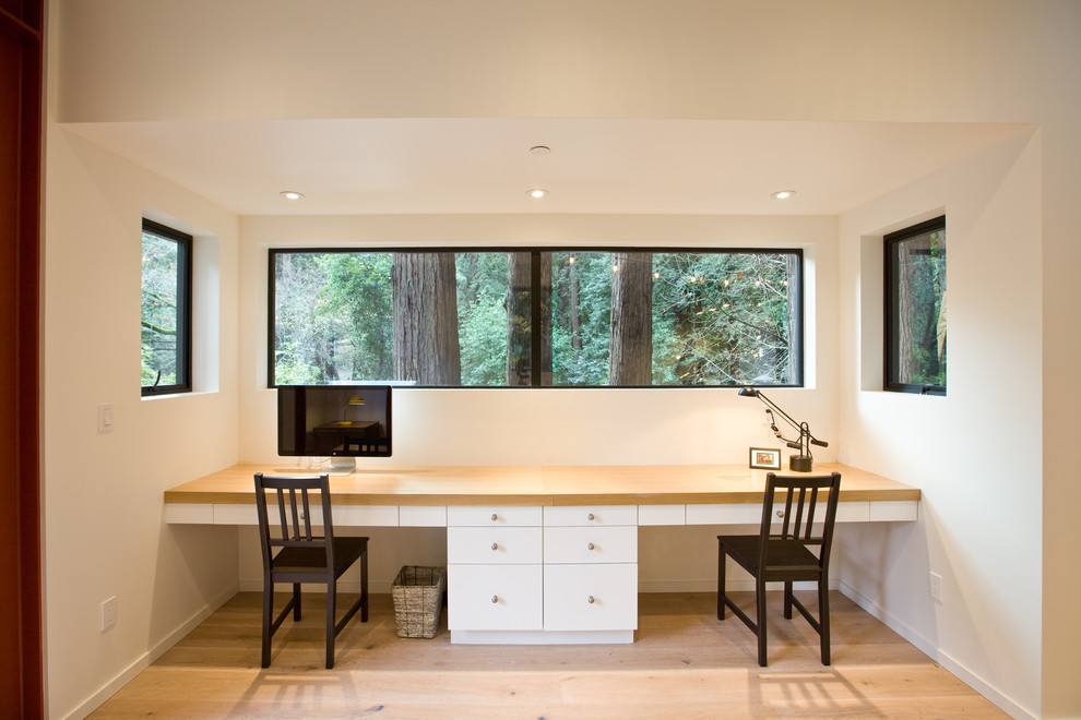 Diseño de despacho minimalista pequeño con paredes blancas, suelo de madera clara y escritorio empotrado