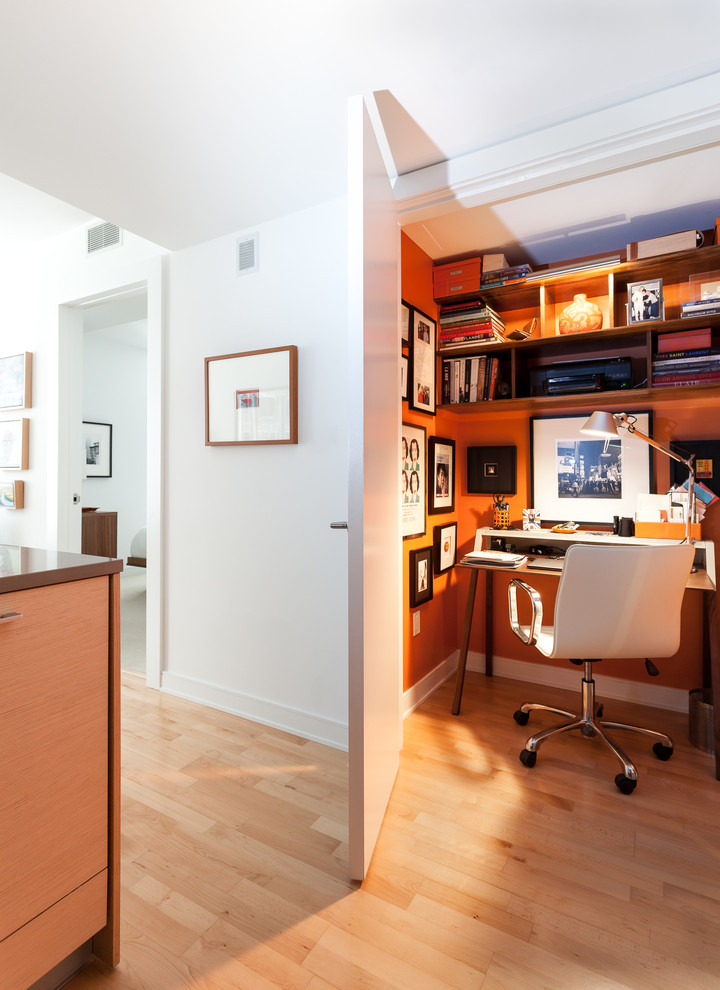 Modern inredning av ett litet arbetsrum, med orange väggar, ljust trägolv och ett fristående skrivbord