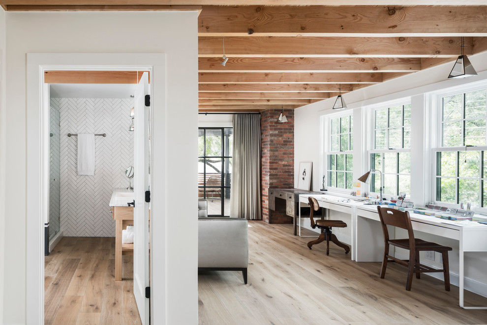 Landhaus Arbeitszimmer mit Arbeitsplatz, weißer Wandfarbe, hellem Holzboden, freistehendem Schreibtisch und beigem Boden in Austin