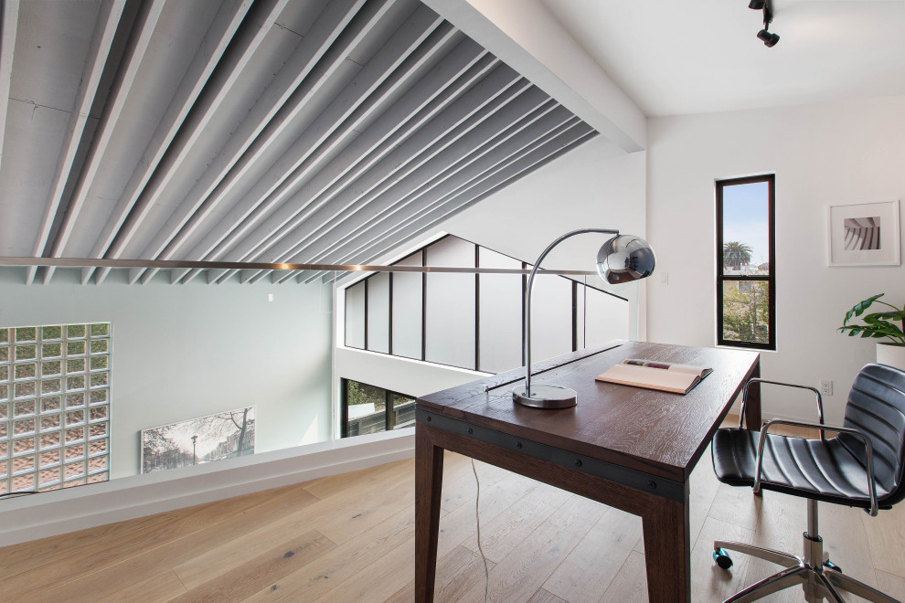 Bild på ett funkis arbetsrum, med vita väggar, ljust trägolv, ett fristående skrivbord och beiget golv