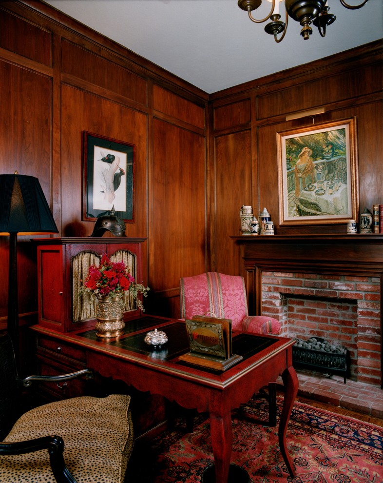 Modelo de despacho tradicional con paredes marrones, suelo de madera en tonos medios, todas las chimeneas, marco de chimenea de ladrillo y escritorio independiente