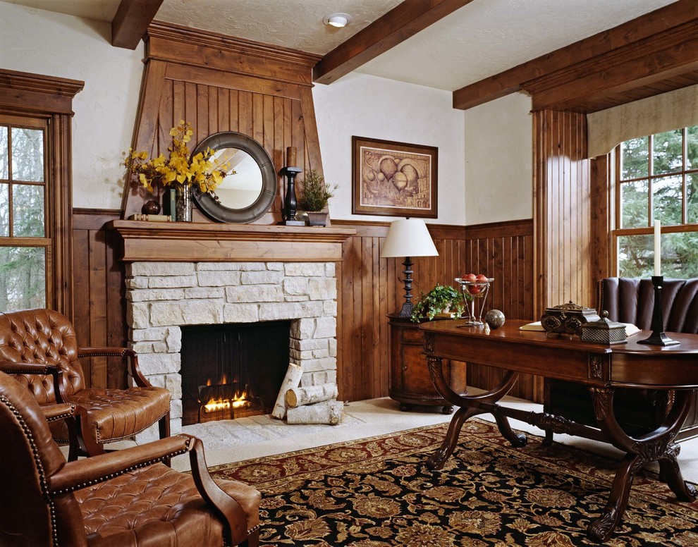 Exempel på ett hemmabibliotek, med beige väggar, heltäckningsmatta, en spiselkrans i sten och ett fristående skrivbord