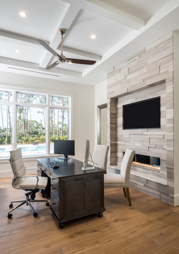 Modernes Arbeitszimmer mit weißer Wandfarbe, braunem Holzboden, Gaskamin, freistehendem Schreibtisch und braunem Boden in Miami