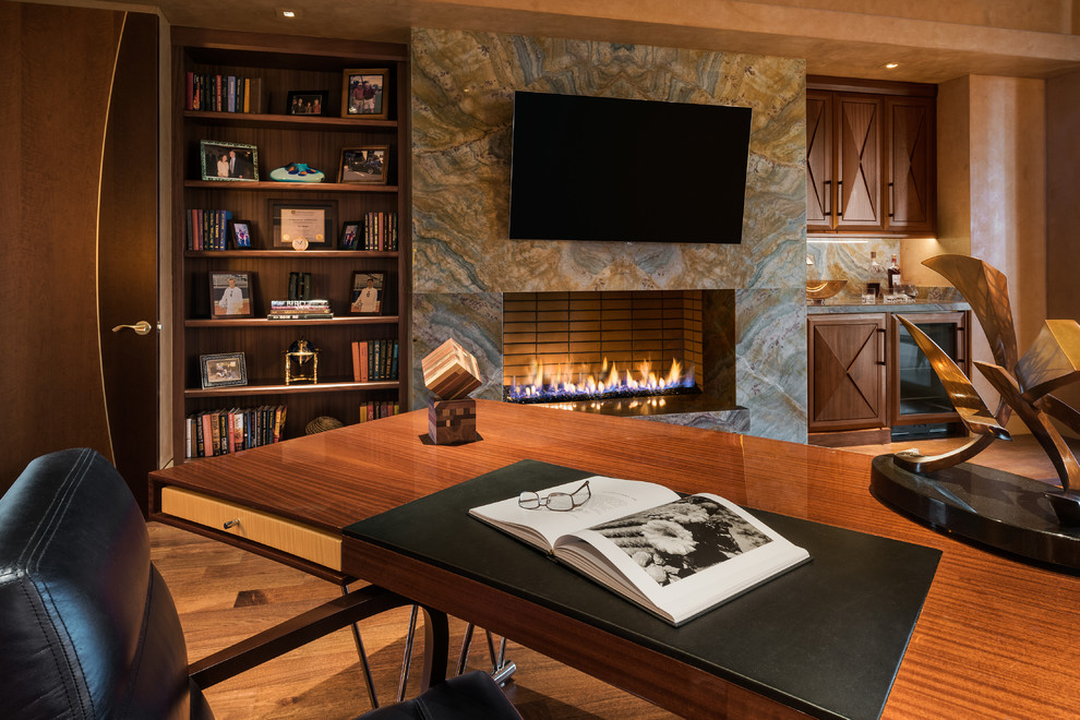 フェニックスにあるラグジュアリーな広いコンテンポラリースタイルのおしゃれな書斎 (茶色い壁、淡色無垢フローリング、横長型暖炉、石材の暖炉まわり、自立型机) の写真